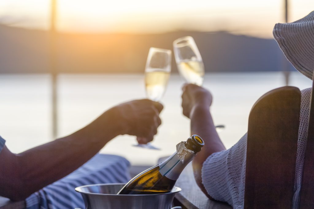 Couple relaxing and drinking champagne on deck chairs on the waterfront.